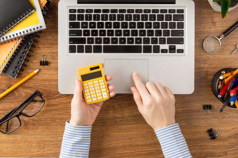 Mulher com calculadora na mão e mexendo em Notebook